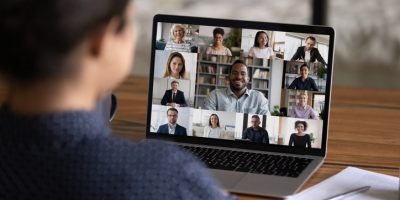 Over shoulder view of female worker have webcam digital virtual conference with diverse multiethnic colleagues. Woman speak talk on video call with multiracial businesspeople. Online meeting concept.